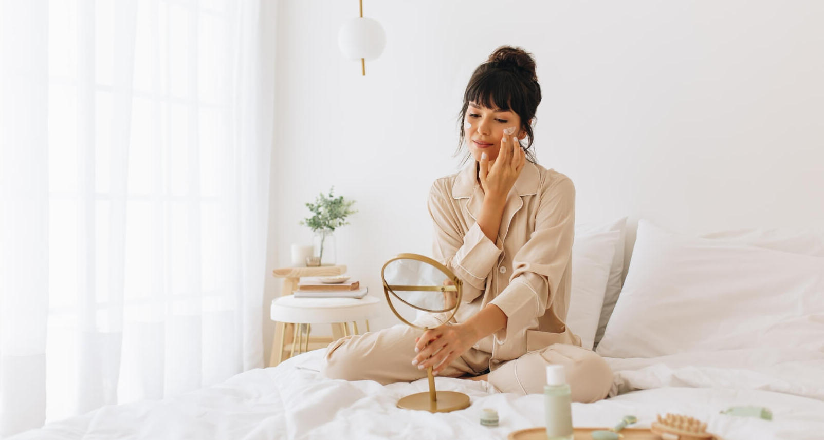 Woman practicing self-care rituals with skincare products by her bed.